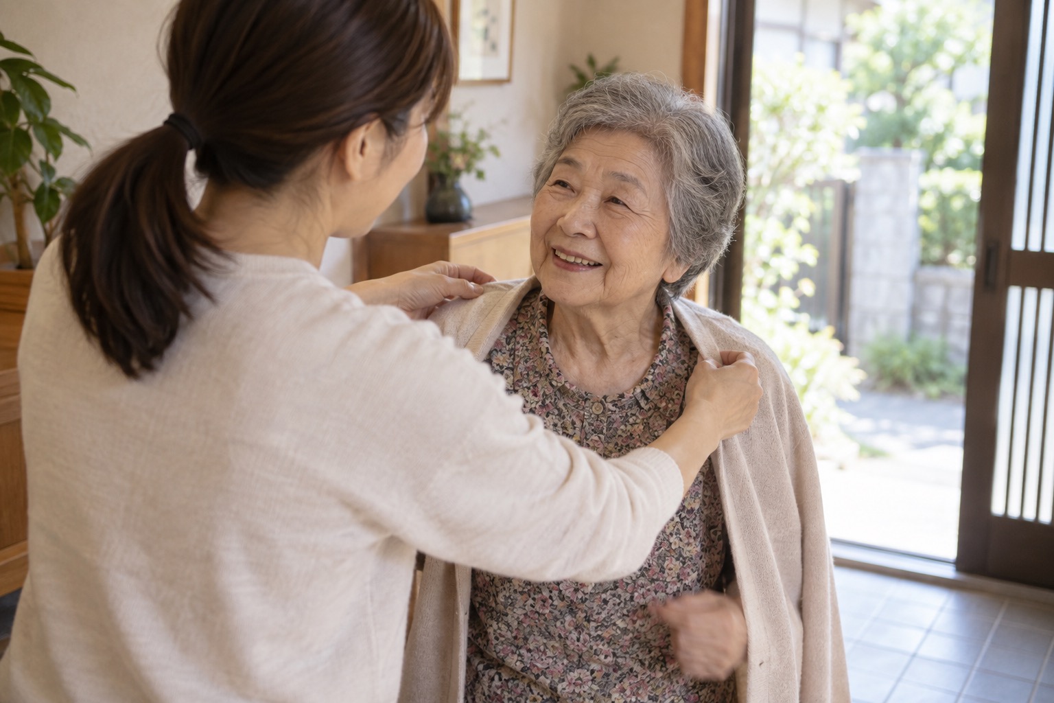 日本の住居の玄関近くで高齢の母の上着を整え外出準備を手伝う娘の編集イメージ写真